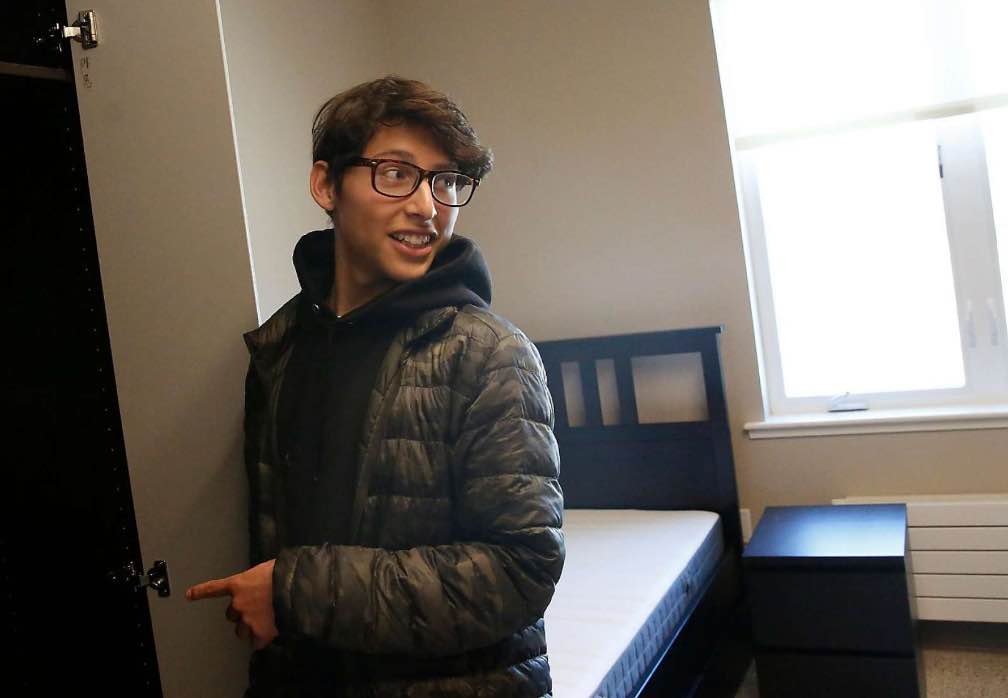 A student smiles pointing to the door of a newly constructed dorm room.