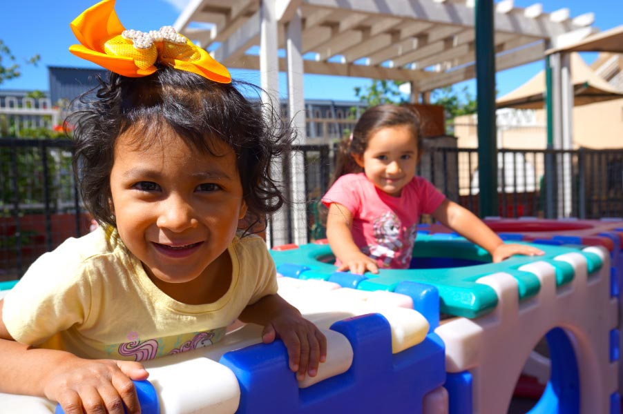 Two children smiling while playing in a plastic playground structure